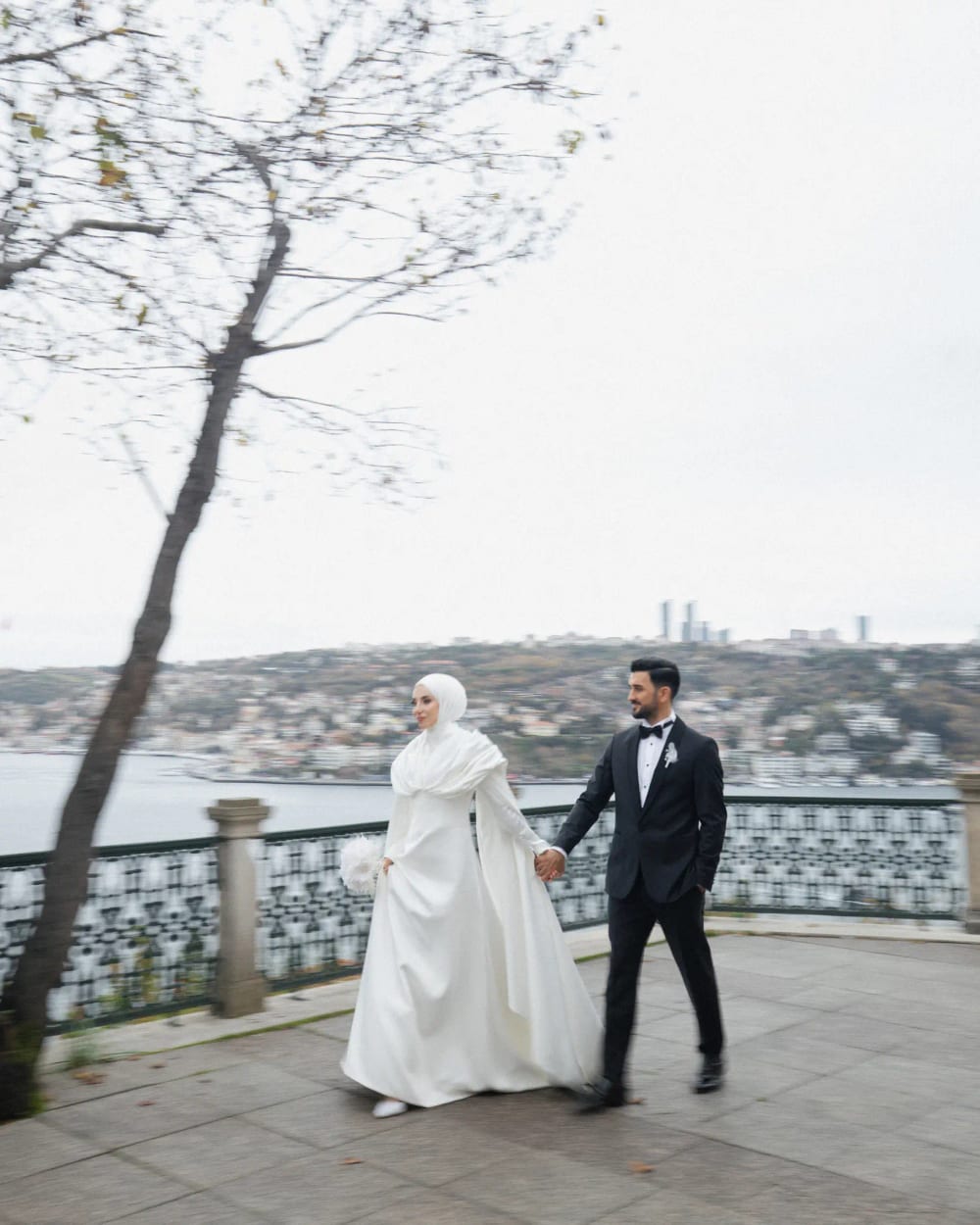 Bride and groom walking hand in hand on the terrace of the Adile Sultan Palace, the Bosphorus behind them