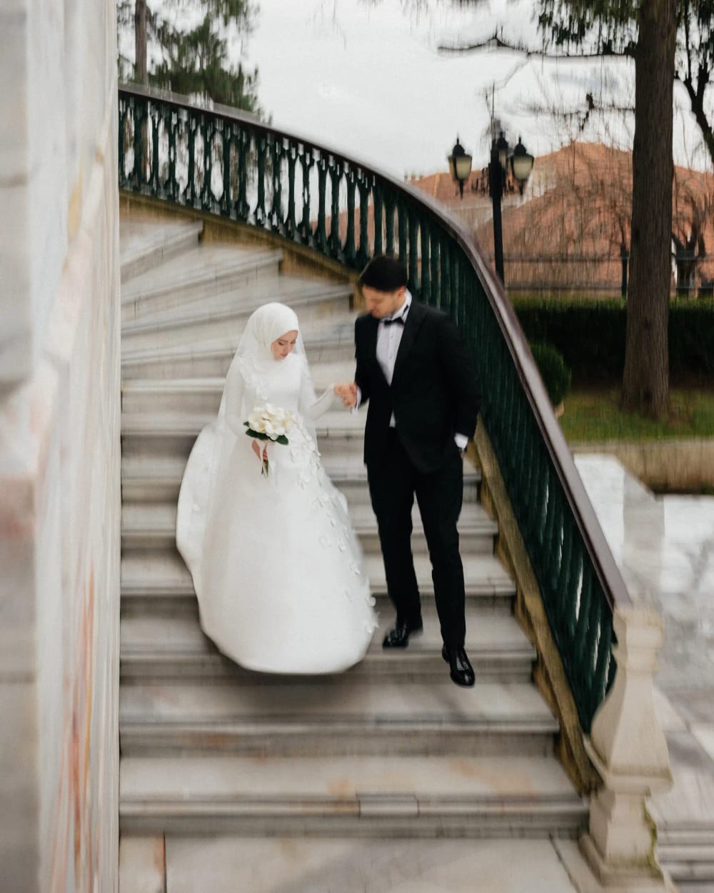 Bride and groom on the marble staircase with wrought-iron railings at the Adile Sultan Palace